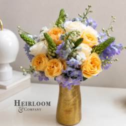 Yellow and white roses with lavender flowers in a gold vase