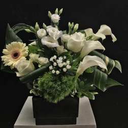 White floral arrangement with calla lilies, roses, and a gerbera daisy in a black vase