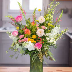 Mixed pink, white, and yellow flowers in a tall green glass vase