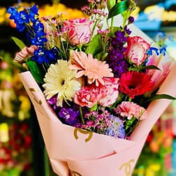 Mixed bouquet with gerbera daisies, carnations, and purple flowers in pink wrap