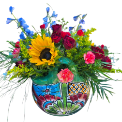 Mixed bouquet with a sunflower, red roses, blue delphinium, and pink carnations in a painted vase.