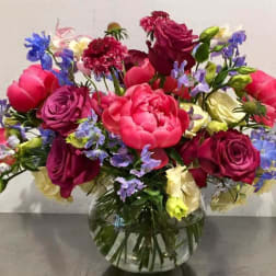 Mixed bouquet of pink, purple, and blue flowers in a clear glass vase