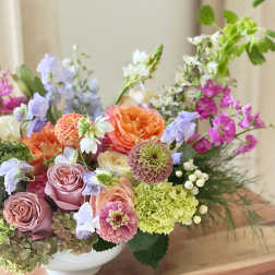 Mixed bouquet of roses, zinnias, hydrangea, and lavender flowers in a white bowl vase