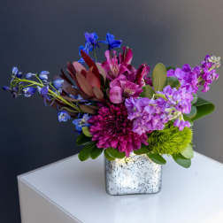Colorful bouquet in a speckled square vase with purple and blue flowers
