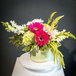 Pink gerbera daisies and white flowers arranged in a pale green vase