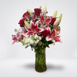 Bouquet of red roses and pink lilies in a green glass vase