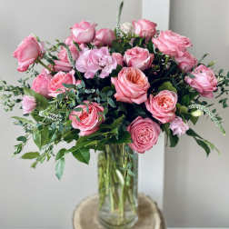 Pink roses arranged in a clear glass vase with greenery