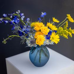 Blue and yellow flower arrangement in a blue glass vase