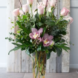 Pink roses and orchids arranged in a tall glass vase