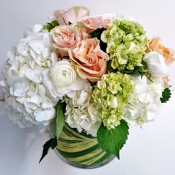 Bouquet of white hydrangeas, peach roses, and green blooms in a glass vase