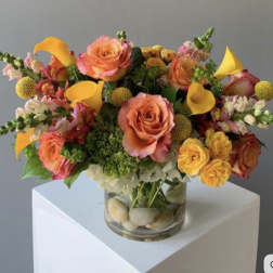 Bouquet of orange and pink roses with yellow calla lilies in a glass vase