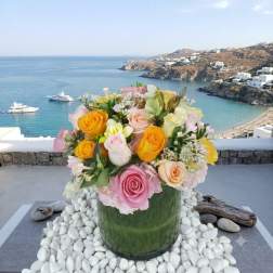 Mixed pastel roses arranged in a green glass vase with white stones