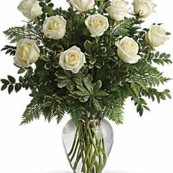 White roses arranged in a clear glass vase with greenery