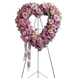 Heart-shaped pink and purple floral wreath on a stand with a ribbon