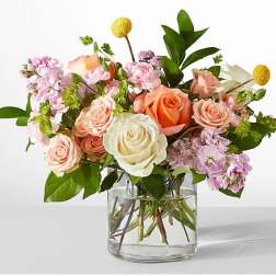 Peach, pink, and white roses with accent flowers arranged in a clear glass vase