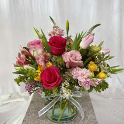 Mixed pink, yellow, and white flowers arranged in a glass vase with a ribbon