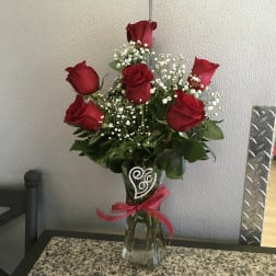 Red roses with baby's breath in a clear glass vase tied with a pink ribbon