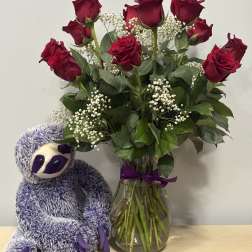 Red roses in a glass vase beside a purple stuffed sloth