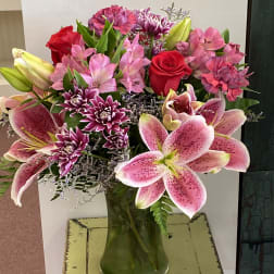 Mixed bouquet of pink lilies, red roses, and purple flowers in a glass vase