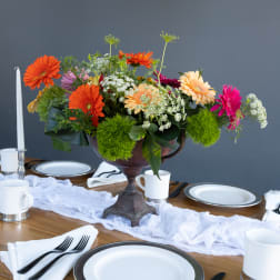 Colorful gerbera daisy centerpiece in a dark pedestal vase on a set dining table