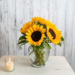 Sunflower bouquet in a glass vase beside a lit candle