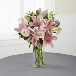 Pink lilies and roses arranged in a clear glass vase