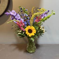 Mixed bouquet with a sunflower and purple, pink, and blue flowers in a glass vase