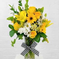 Yellow and white mixed bouquet in a glass vase with a striped ribbon
