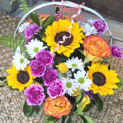 Mixed bouquet with sunflowers, roses, daisies, and carnations under a Happy Birthday topper