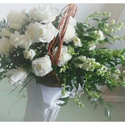 White rose bouquet in a basket-style holder with trailing greenery