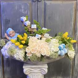 Floral arrangement with yellow tulips, pale roses, and a baby doll.