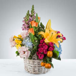 Colorful mixed flower arrangement in a white wicker basket with oranges