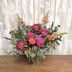 Mixed bouquet of pink, orange, and burgundy flowers in a glass vase
