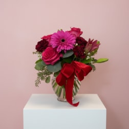 Pink and red flower bouquet in a glass vase with a red ribbon