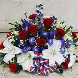 Red roses and white lilies with blue flowers in a patriotic ribboned arrangement