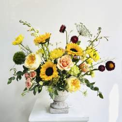 Mixed bouquet with sunflowers, roses, and yellow blooms in a gray pedestal vase