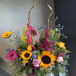 Colorful mixed flower arrangement with sunflowers, roses, and tall stems in a vase