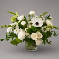White floral arrangement in a clear glass vase with green accents
