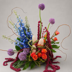 Tall floral arrangement with blue, purple, and orange blooms in a low container