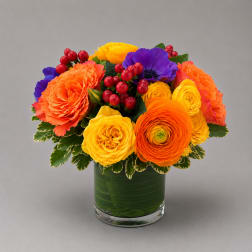 Bright mixed bouquet in a glass vase with orange, yellow, and purple blooms
