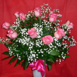 Pink roses and baby's breath in a white vase with a pink ribbon