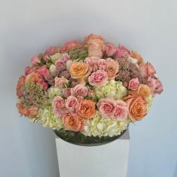 Round bouquet of pink and peach roses with pale hydrangeas in a glass bowl