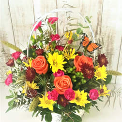 Basket arrangement of orange roses, yellow daisies, and pink flowers with a butterfly pick