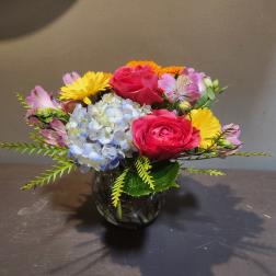 Mixed bouquet with pink roses, blue hydrangea, and yellow daisies in a glass vase