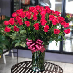 Large bouquet of red roses in a glass vase with a pink ribbon