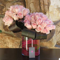 Two bouquets of pale pink roses in a glass vase with black ribbon