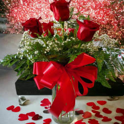 Red roses in a glass vase with a red ribbon and heart confetti