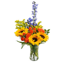 Sunflowers, orange blooms, and blue flowers in a clear glass vase