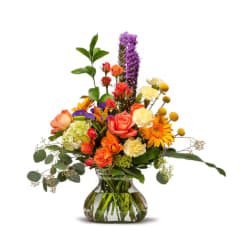 Mixed bouquet of orange, yellow, and purple flowers in a glass vase