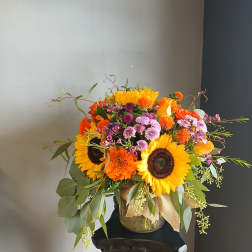 Bouquet of sunflowers, orange blooms, and pink flowers in a glass vase